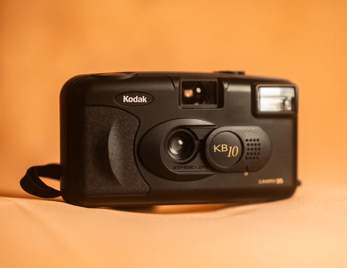The front of the Kodak KB10: aspheric lens, gold KB10 badge, viewfinder and flash, with the wrist strap beside it.