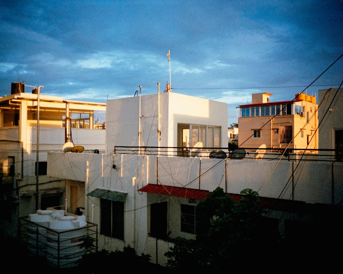 Whitewashed rooftops at dusk, water tanks and satellite dishes against a deep blue sky.