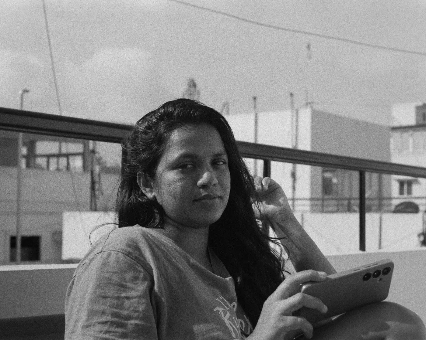A black and white photograph of a person on a rooftop holding a phone, turning to look at the camera.